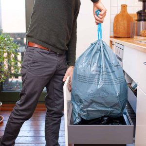 Ein Mann hebt einen vollen 35 Liter Zugband-Müllbeutel, gefüllt mit Restmüll am Zugband aus dem Küchen-Mülleimer